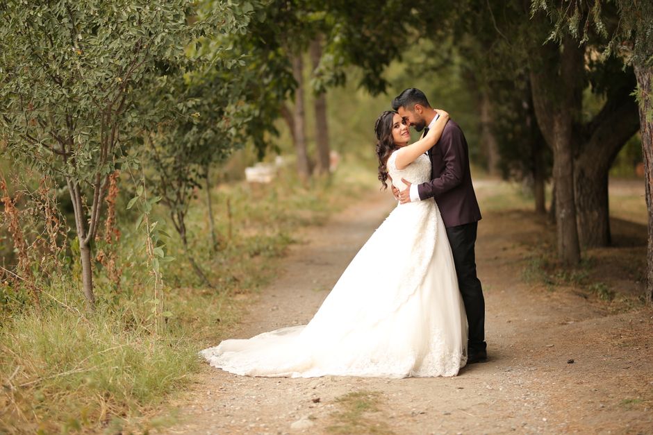 A couple shares a tender embrace on a scenic outdoor path, dressed in wedding attire.