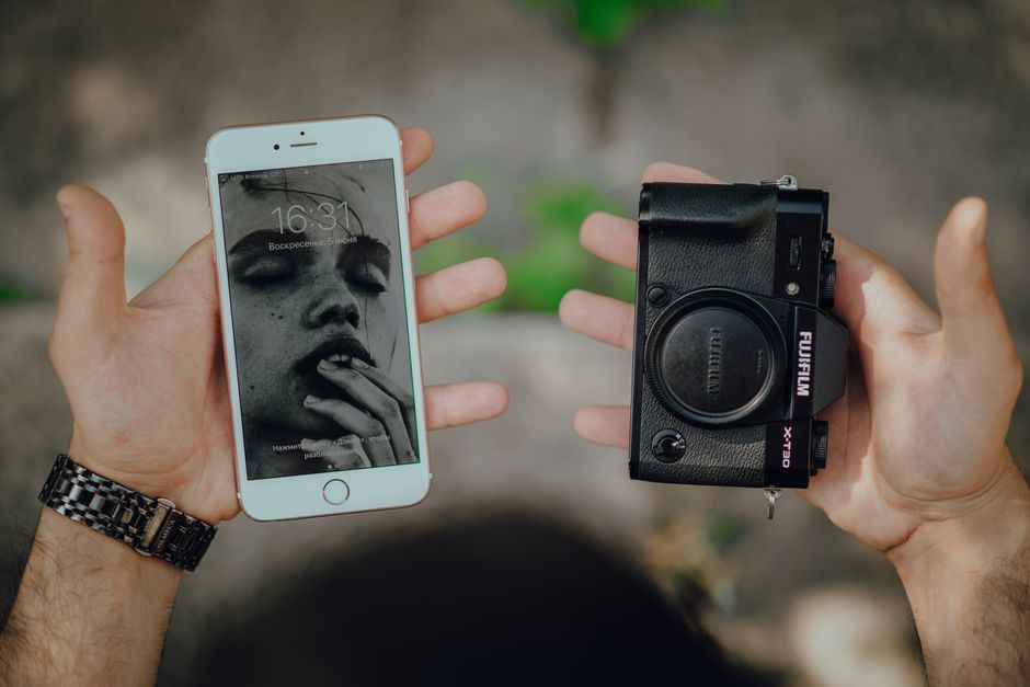 Hands holding a smartphone with art wallpaper and a camera body outdoors.