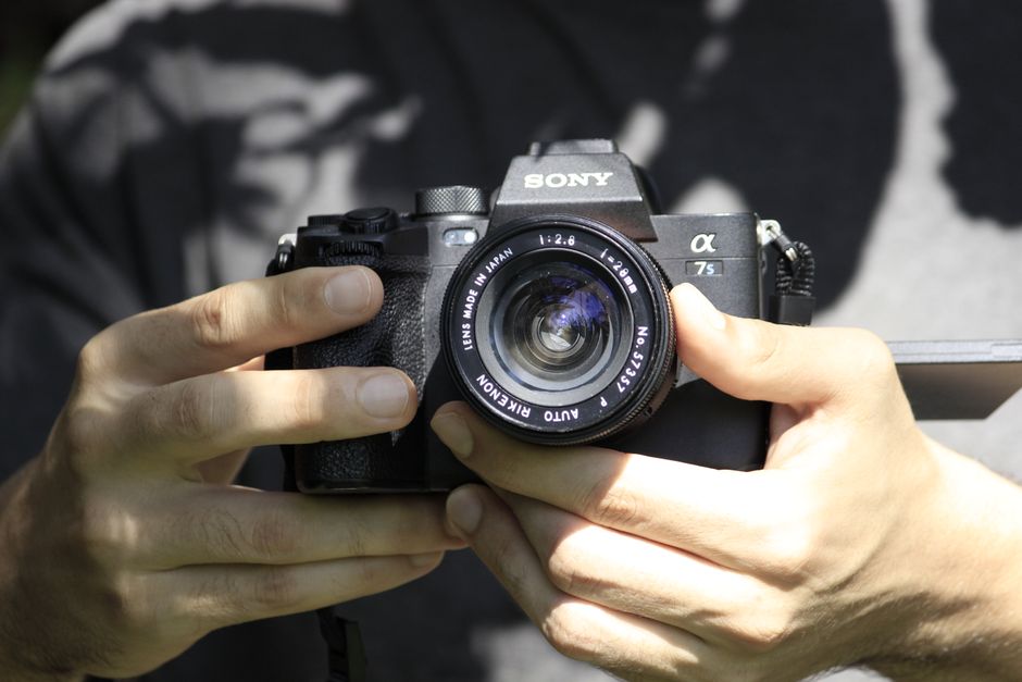Close-up of a person holding a Sony mirrorless camera outdoors in daylight.