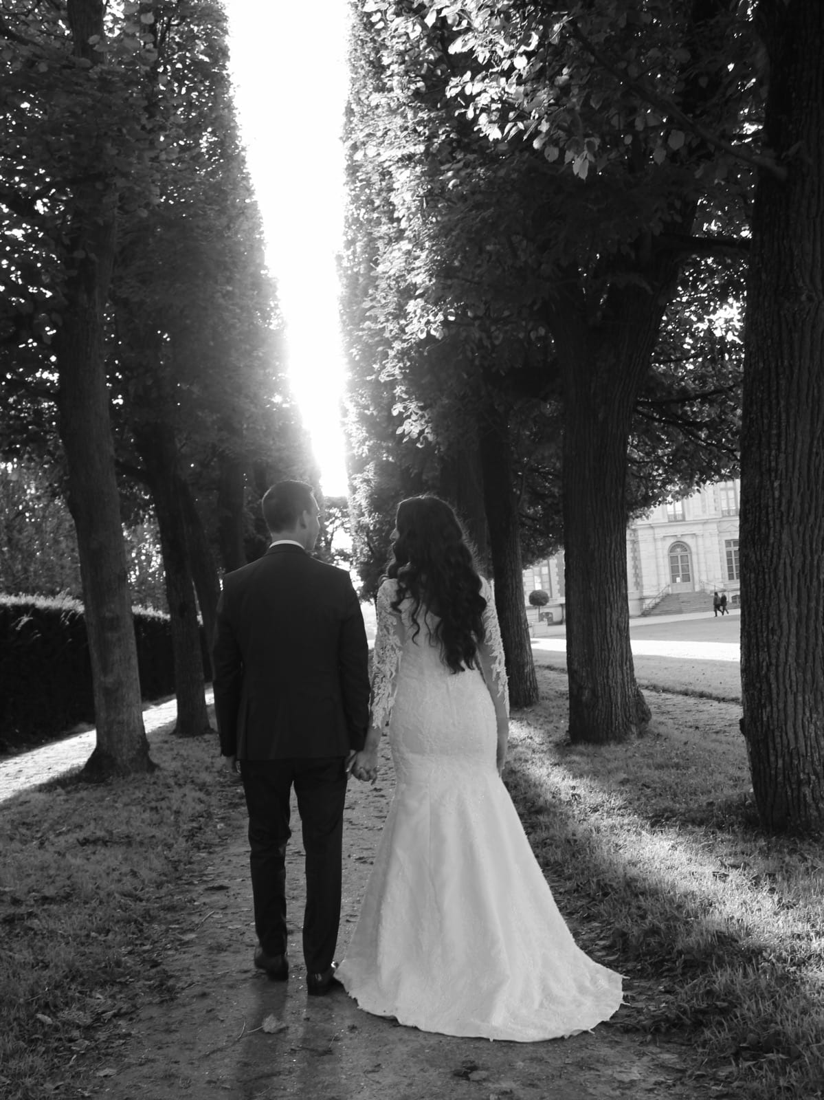 Les mariés s'éloignent main dans la main sous les arbres, en noir et blanc