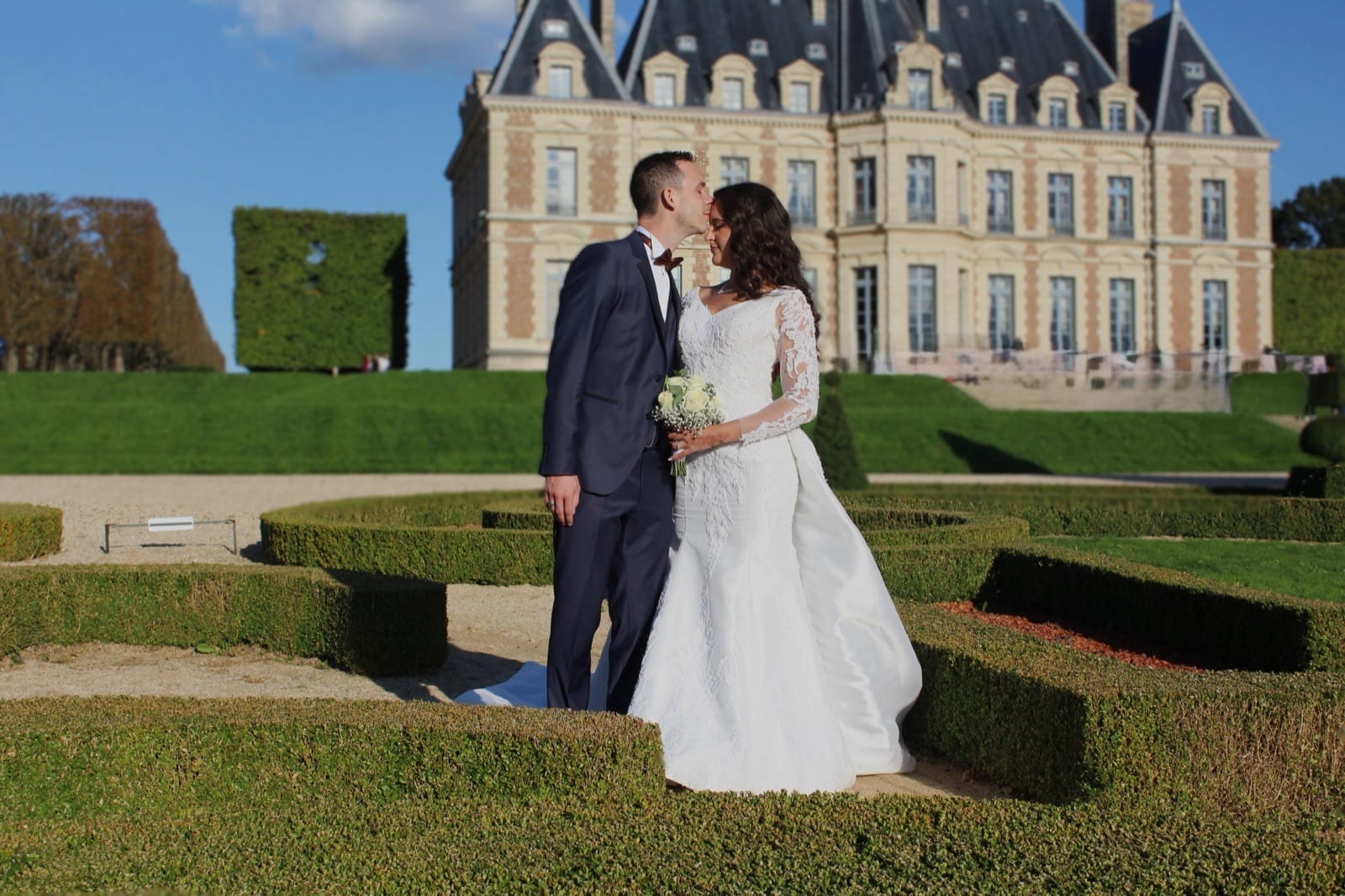 Les mariés devant la façade d'un château, dans un jardin à la française