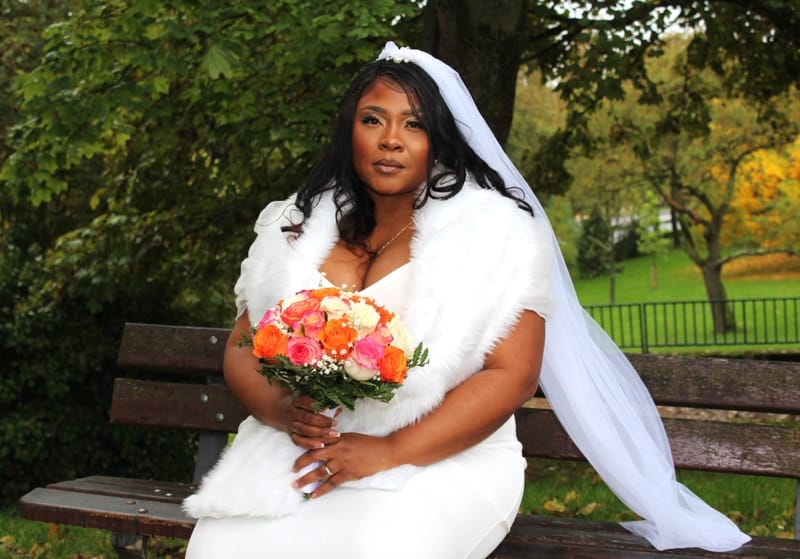 La mariée assise sur un banc, son bouquet à la main, dans un parc d'automne