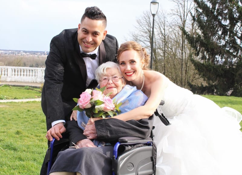 Les mariés entourent une grand-mère en fauteuil roulant, dans le parc